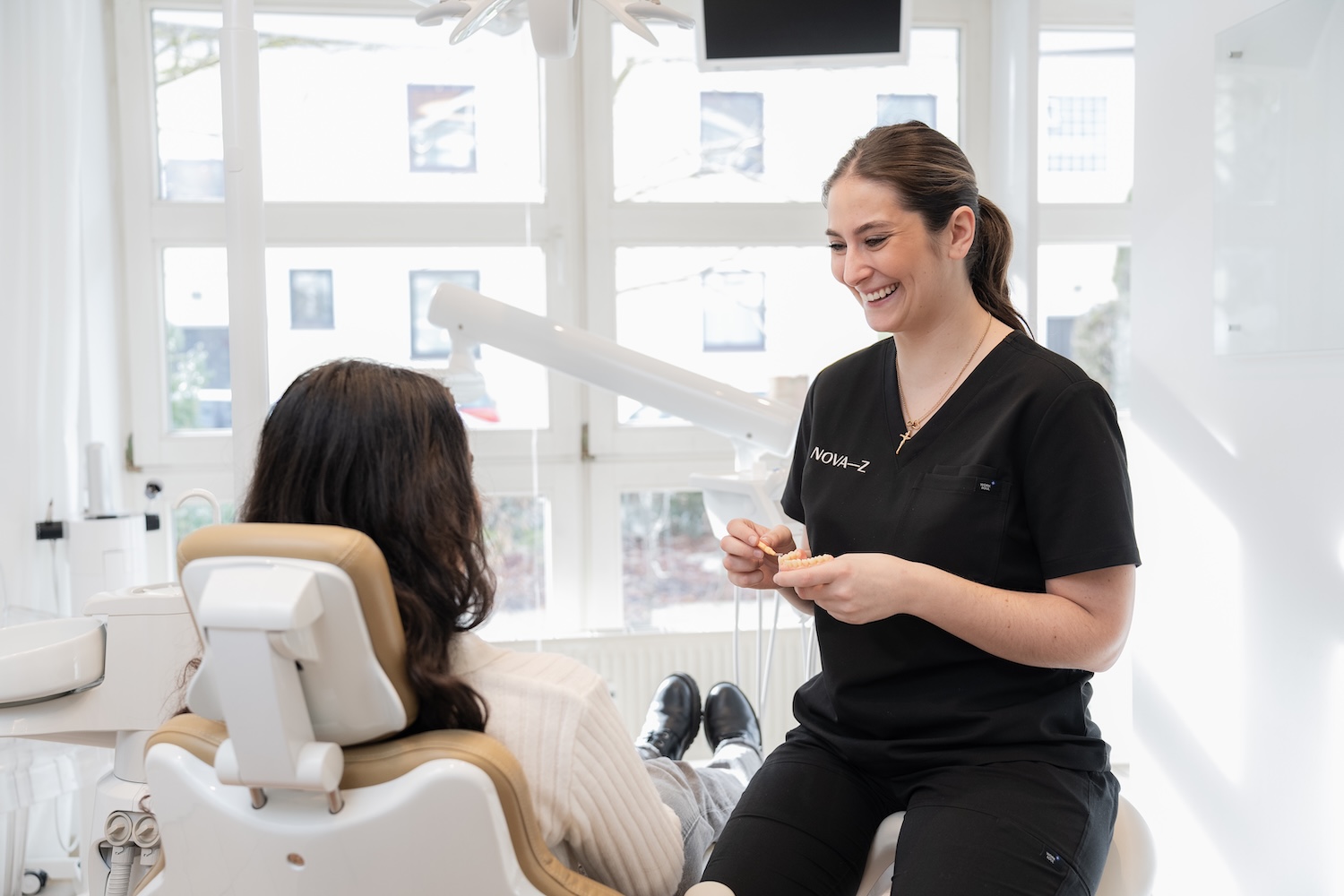 Eine Prophylaxe-Fachkraft von NOVA-Z im Gespräch mit einer Patientin bei einer Vorsorgeuntersuchung. Sie lächelt sehr freundlich.